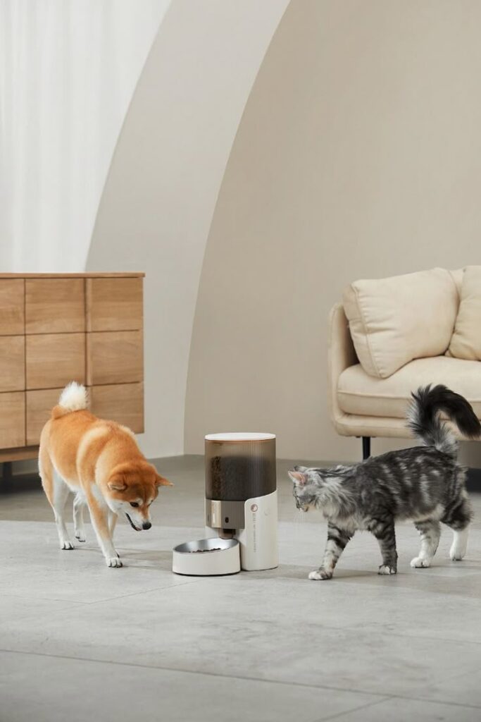 Dog and cat exploring an automatic pet feeder in a modern living room setting.