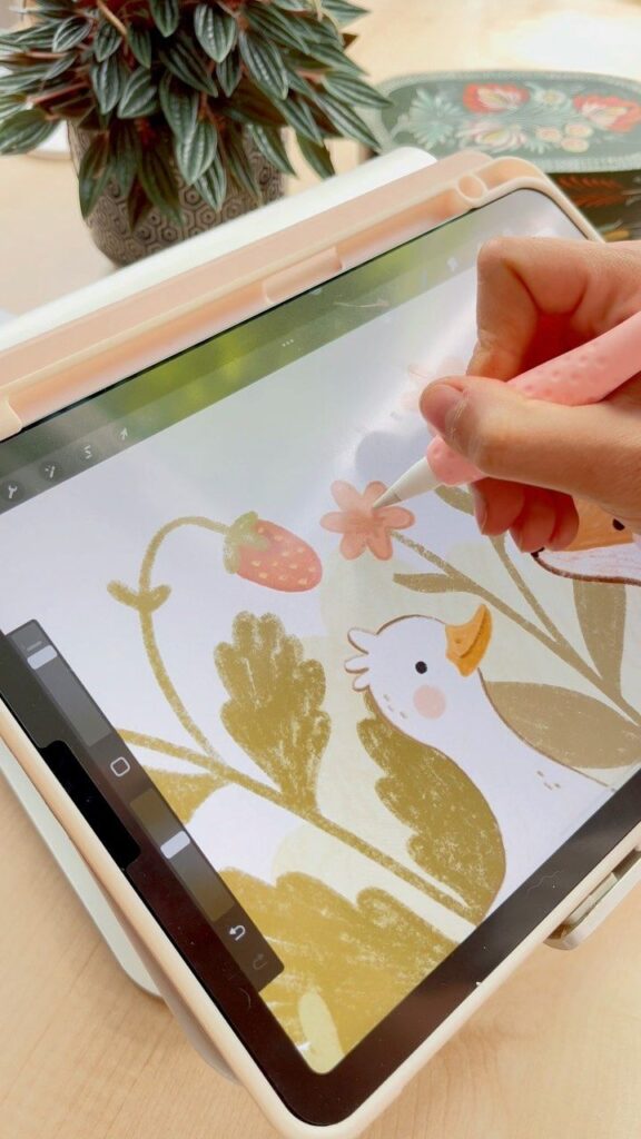 Hand drawing digital art of a duck, strawberry, and flower on a tablet with a plant nearby.