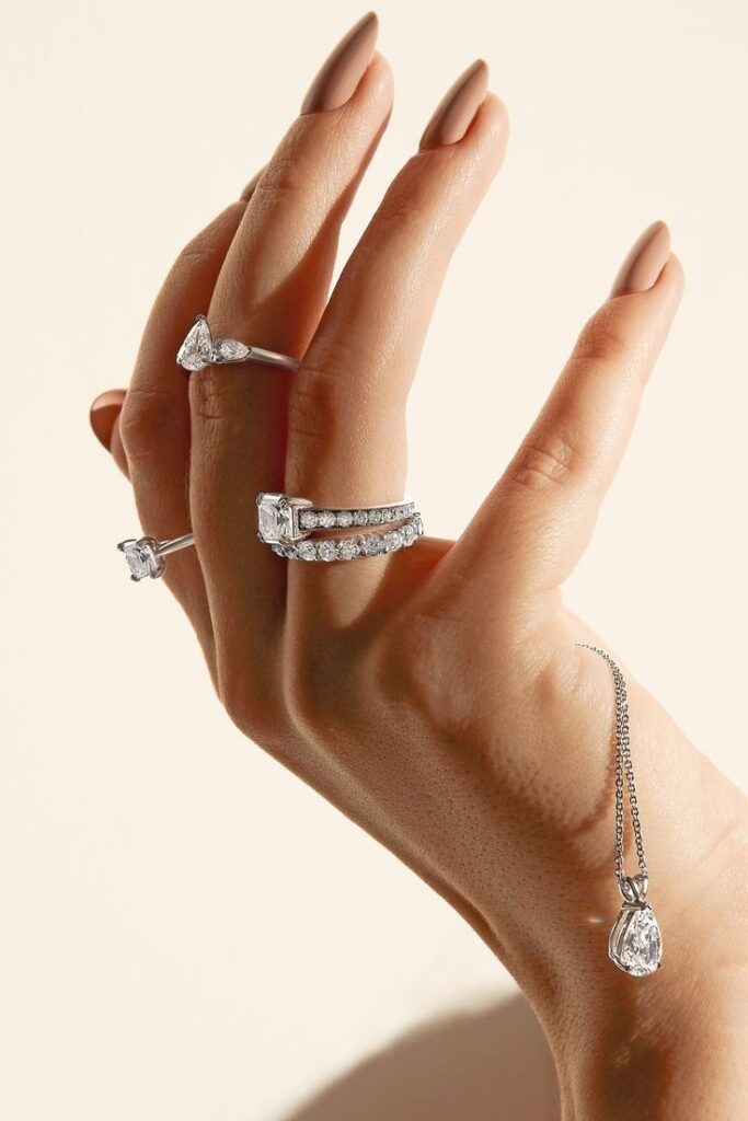 Elegant hand showcasing gold rings and diamond necklace on neutral background.