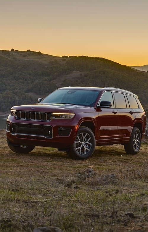 Red SUV parked in a scenic mountain landscape at sunset, highlighting its sleek design and rugged capability.