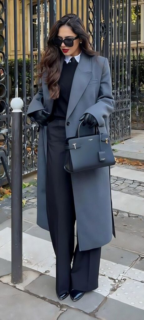 Stylish woman in a gray coat with sunglasses and handbag, standing elegantly on the street.