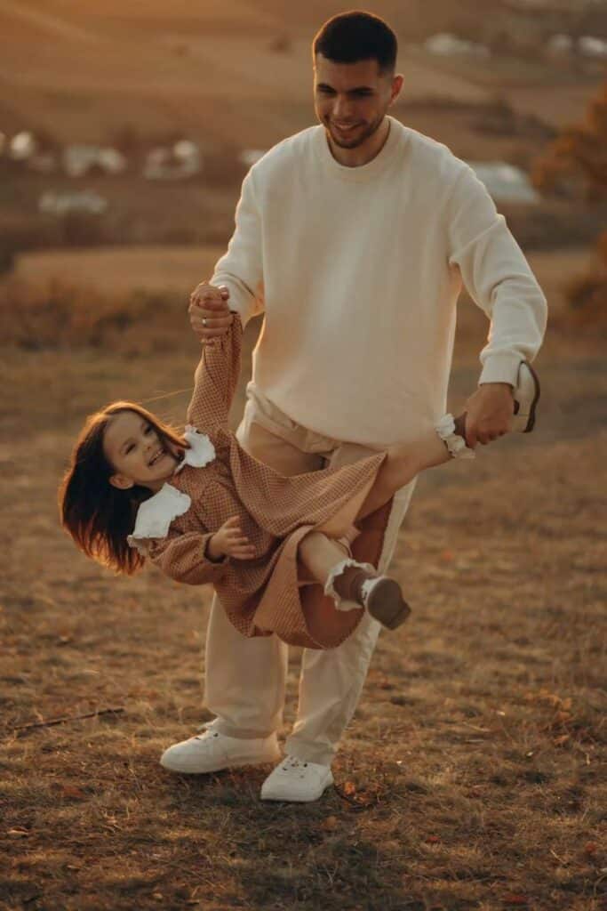 Father playing with daughter outdoors, lifting her playfully in a sunlit field.