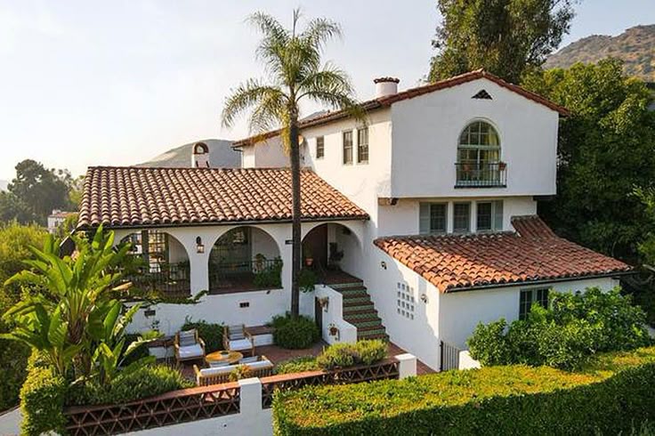 Spanish-style villa with terracotta roof, lush garden, and outdoor seating in scenic hillside setting.