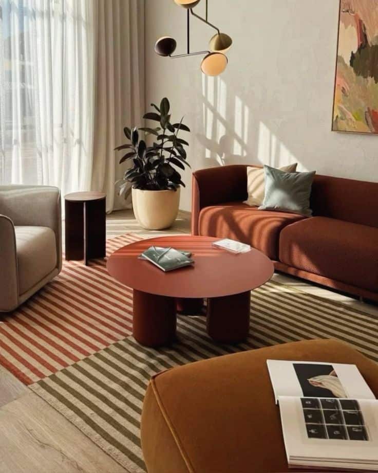 Modern living room with a red coffee table, striped rug, cozy seating, and unique lighting.