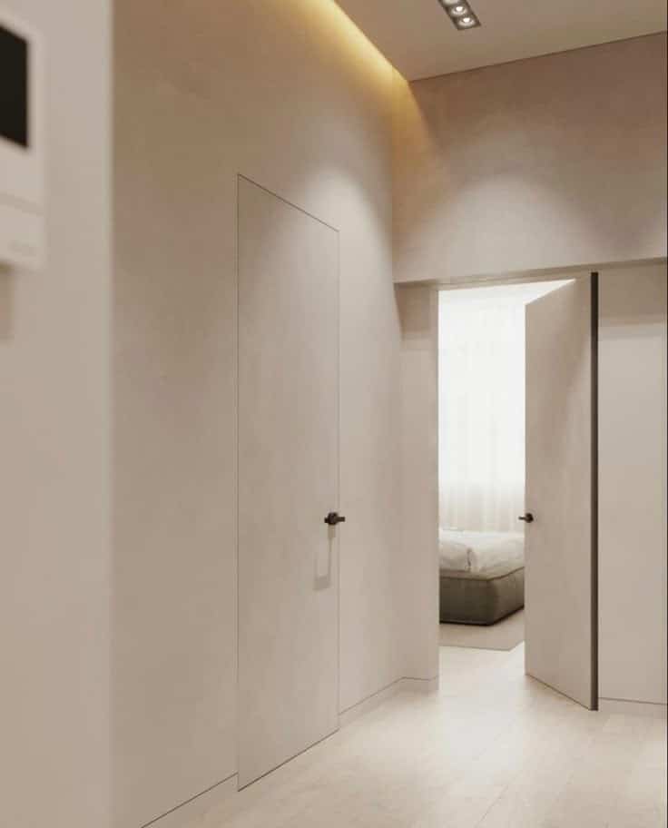 Modern minimalist hallway with open doors leading to a bright bedroom, featuring neutral tones and sleek design.