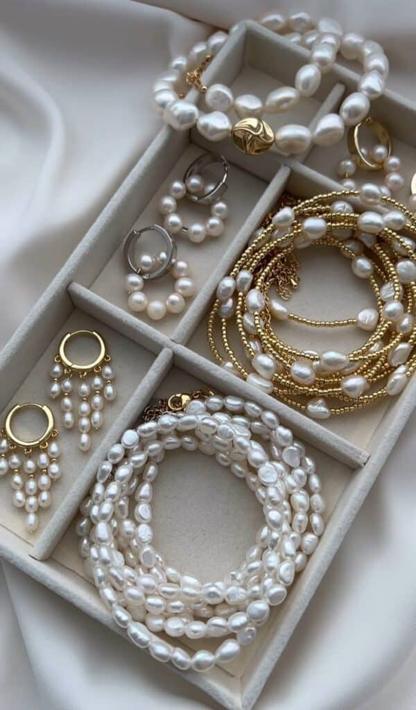 Elegant pearl and gold jewelry set in organizer, featuring necklaces, bracelets, and earrings on silk fabric.