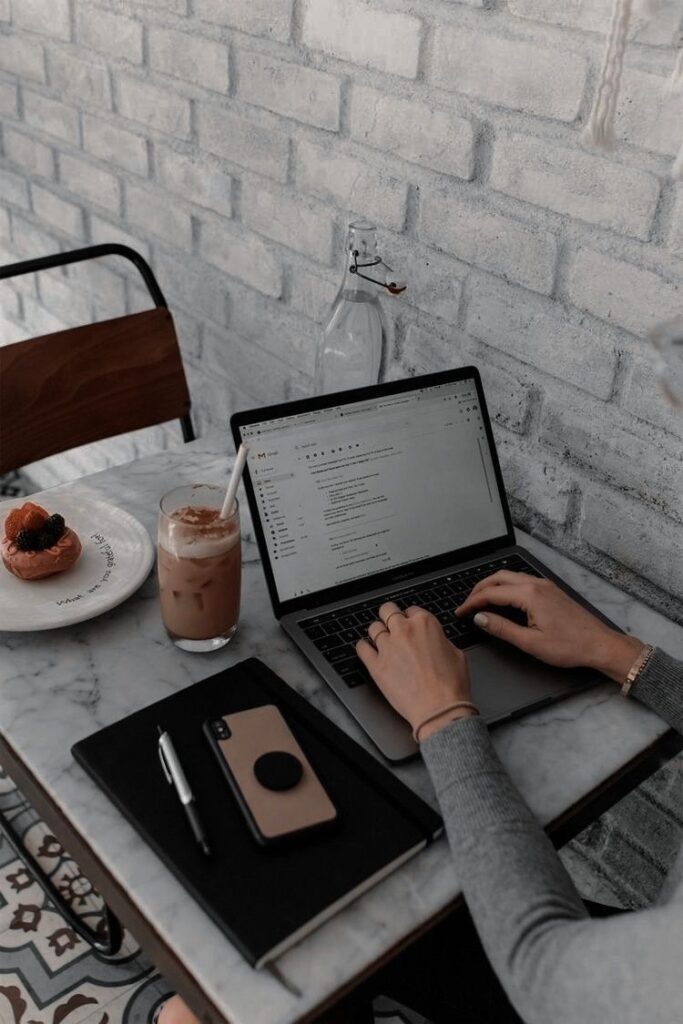 525128f54d8dcb72c6fd94e93c8c5a31 Person typing on laptop at café table with iced coffee and pastry beside them. | Sky Rye Design Person typing on laptop at café table with iced coffee and pastry beside them.