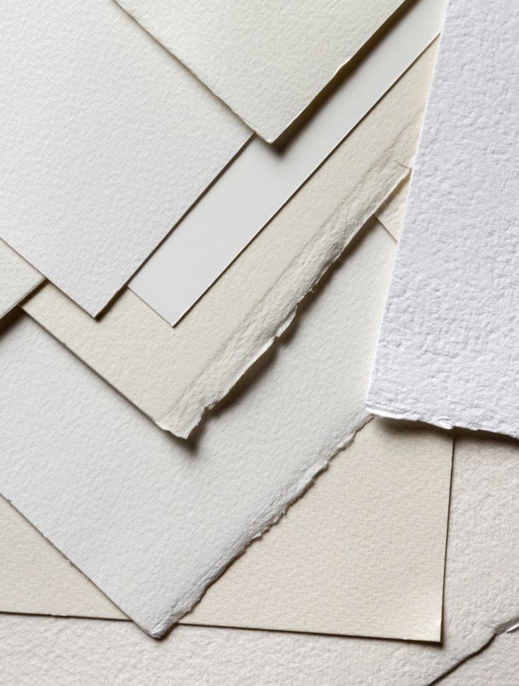 Assorted textured paper sheets in neutral tones layered on top of each other, showcasing different finishes and edges.