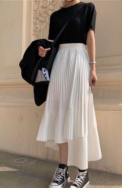 Casual outfit with black tee, white pleated skirt, and sneakers in stylish street fashion look.