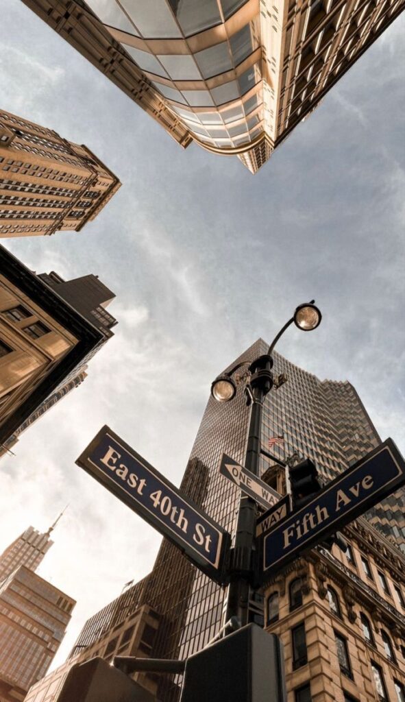 Street signs at East 40th St and Fifth Ave, surrounded by skyscrapers against a clear sky in New York City.