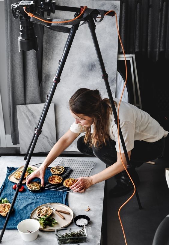 Food photographer styling quiches on a table for a shoot with a professional camera setup.