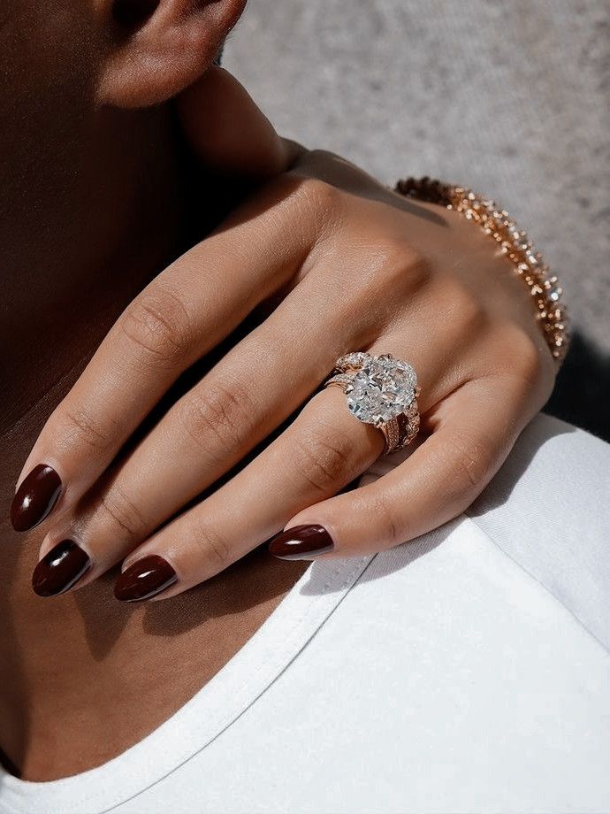 Close-up of a diamond engagement ring on a woman's hand with burgundy nails resting on a shoulder.