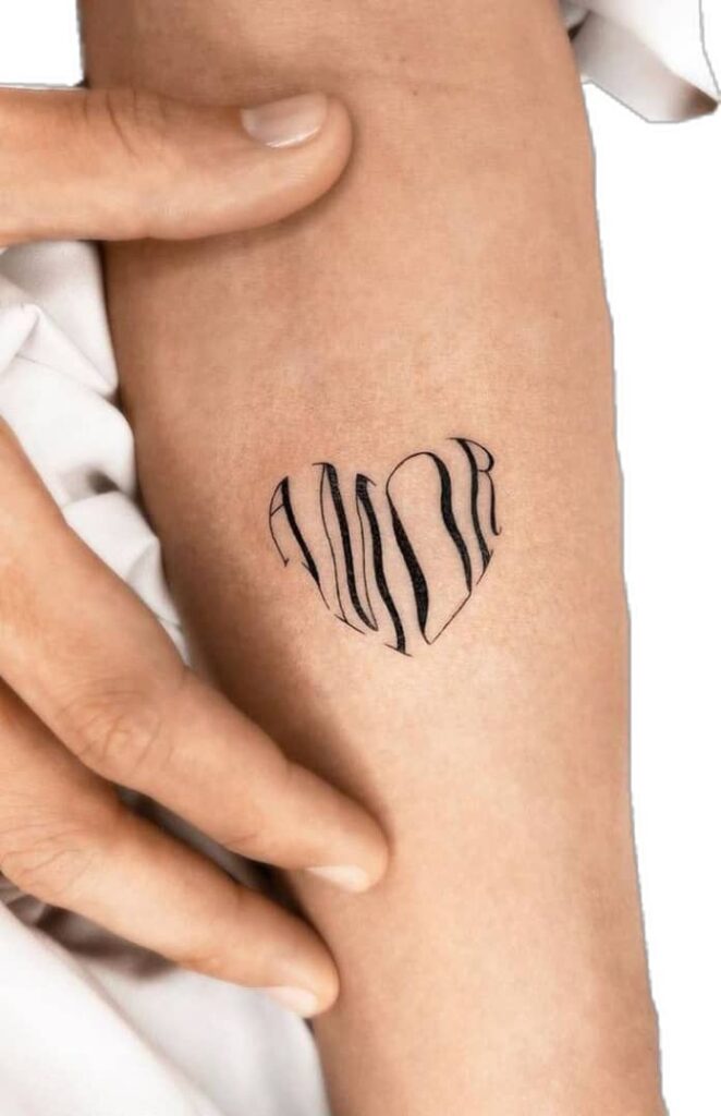 Close-up of a Amor heart tattoo on forearm, minimalist black ink design. Hand touching skin gently.
