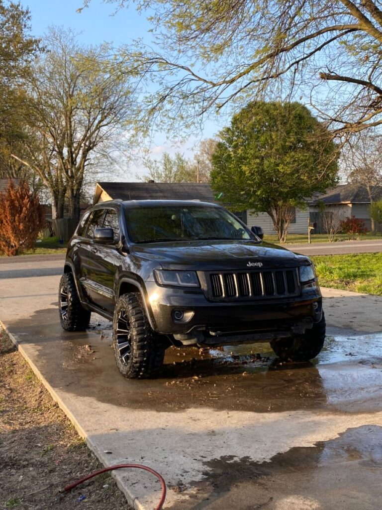 Black SUV on driveway, freshly washed, surrounded by trees and houses in a suburban neighborhood.