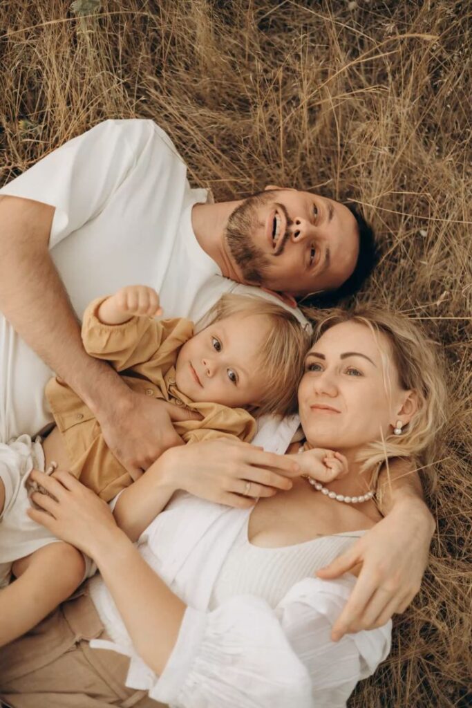 Happy family of three lying on grass, smiling and enjoying nature together in a warm, loving embrace.