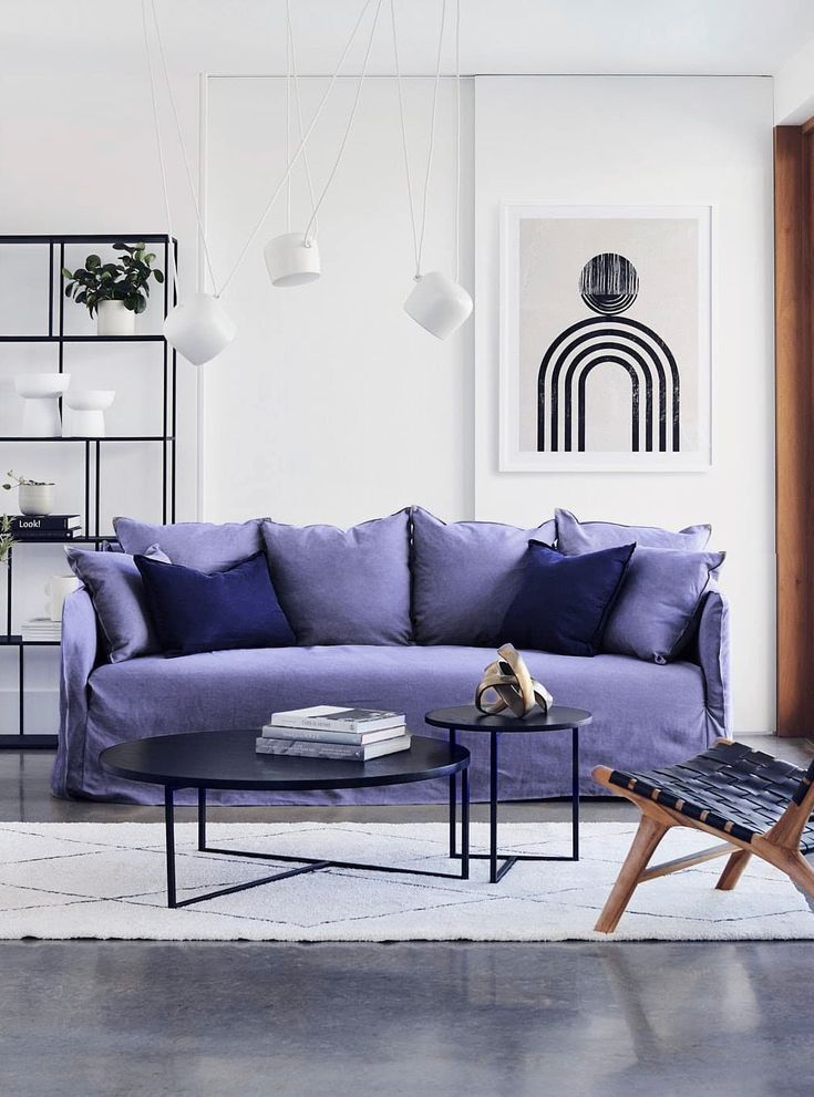 Modern living room with a purple sofa, stylish decor, abstract art, and minimalist lighting fixtures.
