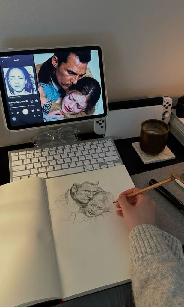 Artist sketching scene from tablet, with music playing and coffee on desk.