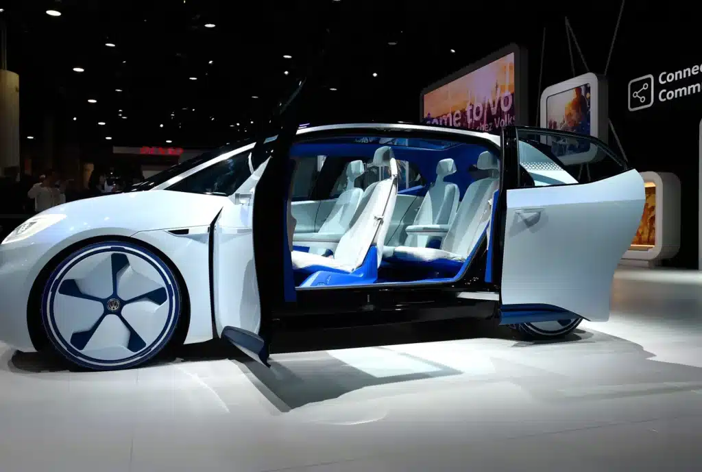 Futuristic white electric car with open doors and sleek interior design displayed at an auto show.