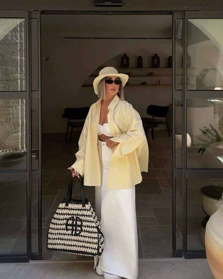 Stylish woman in summer outfit, yellow shirt, wide hat, with a black and white bag, casual elegance.