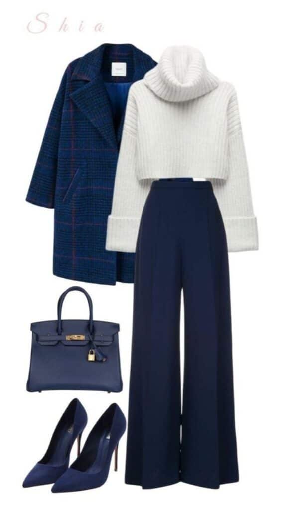 Stylish winter outfit with navy coat, white sweater, blue pants, matching heels, and handbag. Fashionable ensemble.