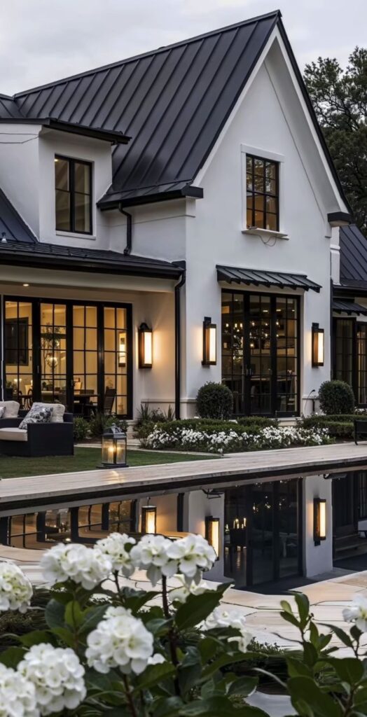 Modern white house with large windows, black roof, garden, and reflecting pool at dusk.