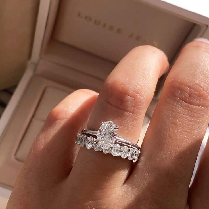 Elegant diamond engagement and wedding rings on a finger, with a jewelry box in the background.