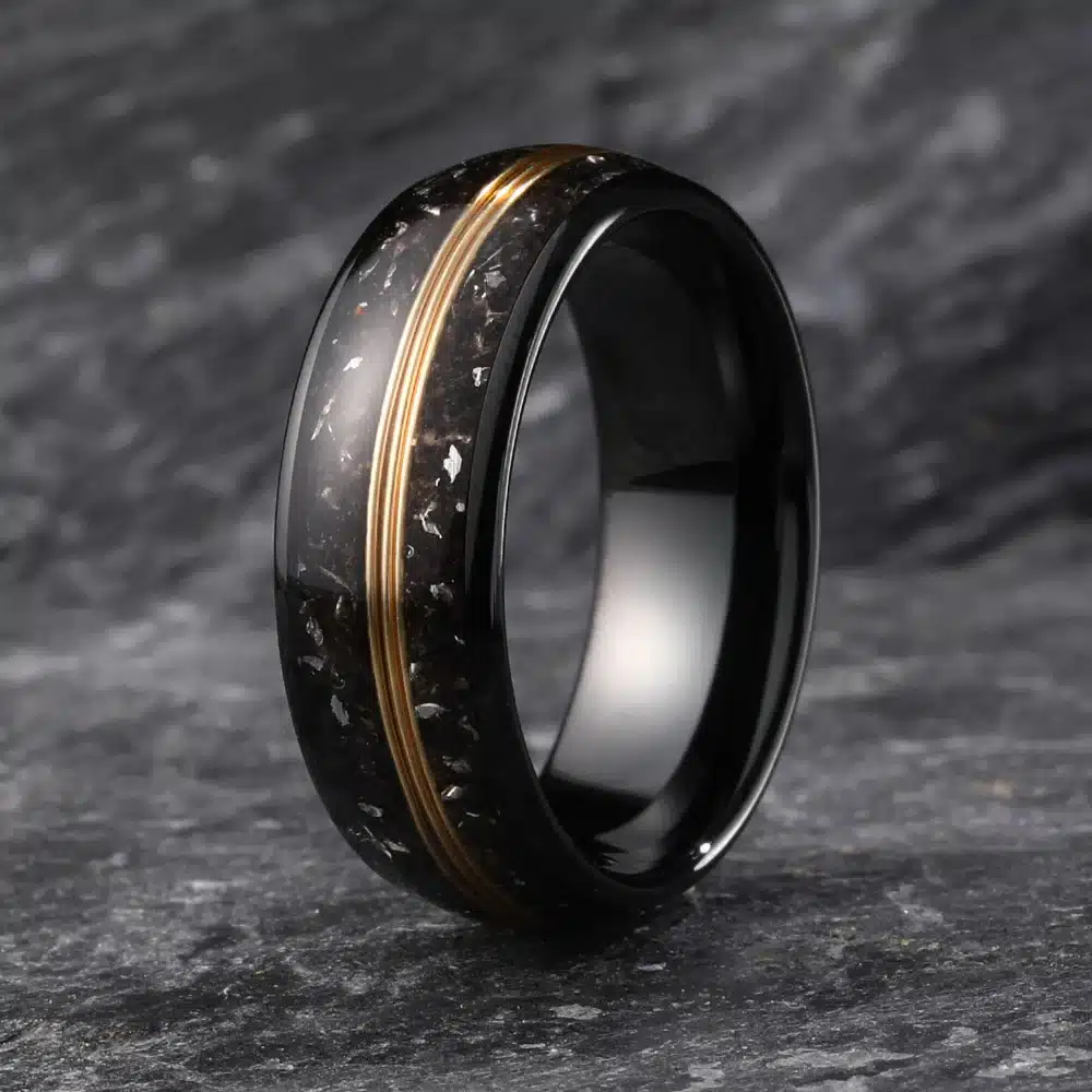 Black tungsten ring with gold accents and speckled detail on a stone background.
