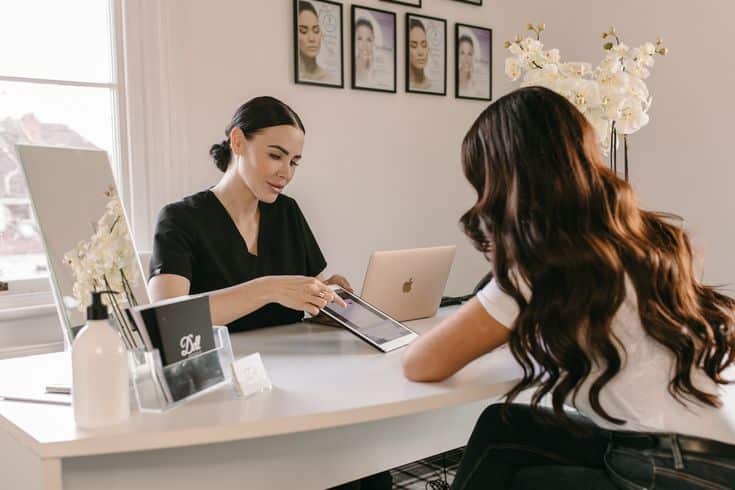Beauty consultant discussing skincare solutions with a client at a clinic, modern decor in background.