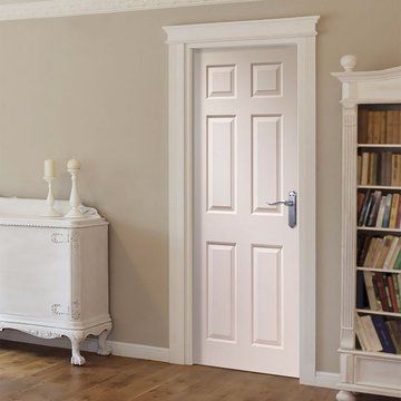 White interior door in a cozy room with a wooden floor, next to a vintage cabinet and a filled bookshelf.
