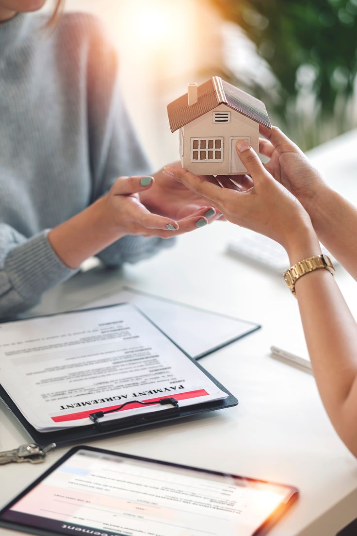 Hands exchanging a miniature house over a payment agreement, symbolizing real estate or property transaction.