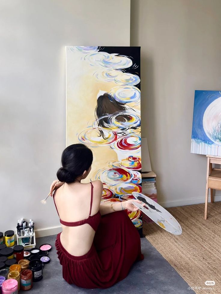 Artist in red dress painting colorful abstract art on canvas in studio.