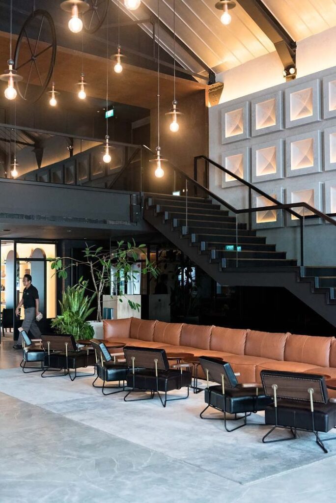 Modern lounge area with leather seating, industrial lighting, and staircase in a spacious interior design setting.