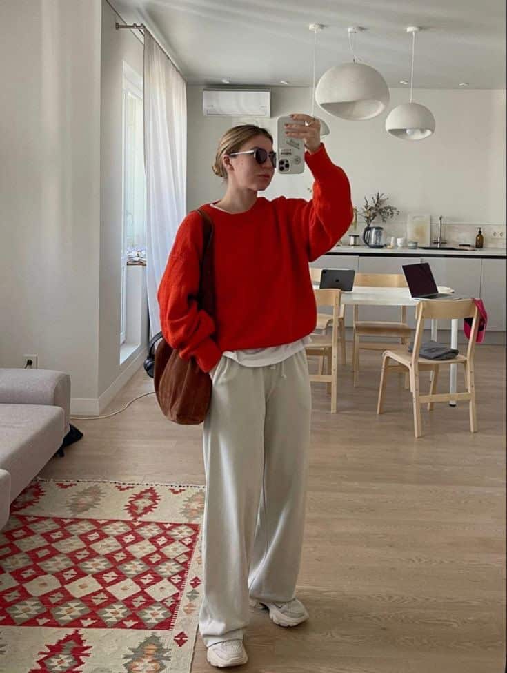Casual outfit with red sweater and white pants in modern living room decor, woman taking a selfie.