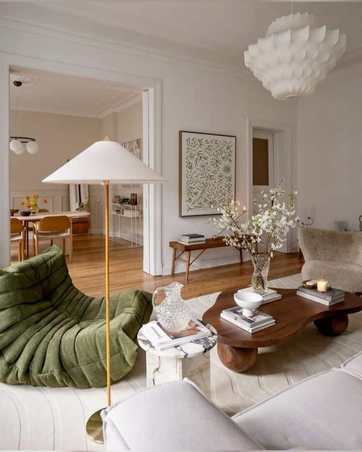 Modern living room with green chair, wooden table, and floral decor, featuring stylish lighting and natural tones.