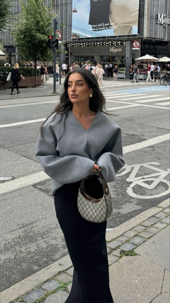 Fashionable woman in city street wearing gray sweater and holding designer bag. Urban style and street fashion.