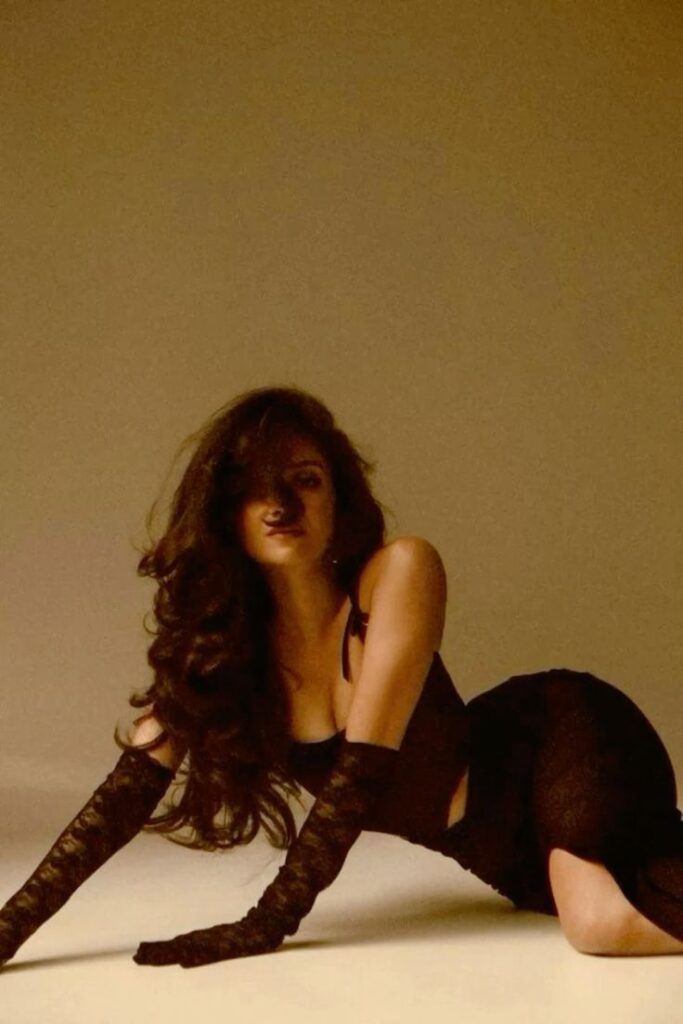 Woman in black dress and gloves poses on the floor, exuding elegance and confidence in soft lighting.