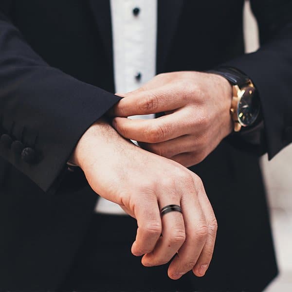 Man adjusting watch and cufflinks on a black suit, showcasing elegant men's fashion.