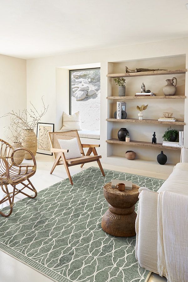 Cozy minimalist living room with a patterned rug, wicker chairs, and wooden shelves showcasing decor items in natural tones.