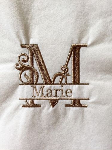 Embroidered letter M with Marie in elegant, brown script on white fabric.