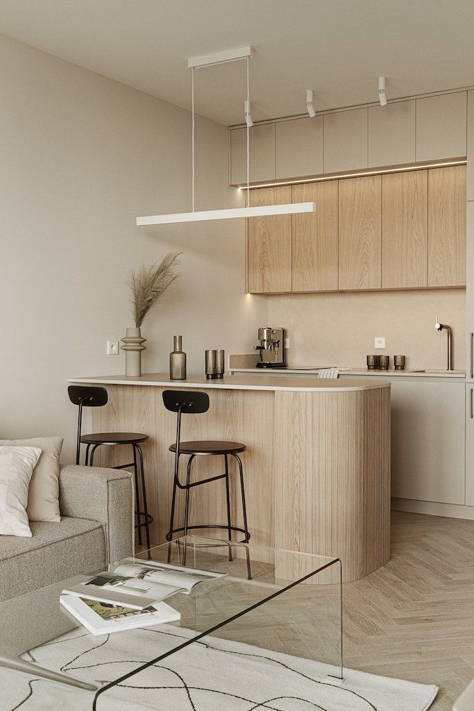 Modern minimalist kitchen with bar stools, light wood cabinets, pendant lighting, and a cozy living area.
