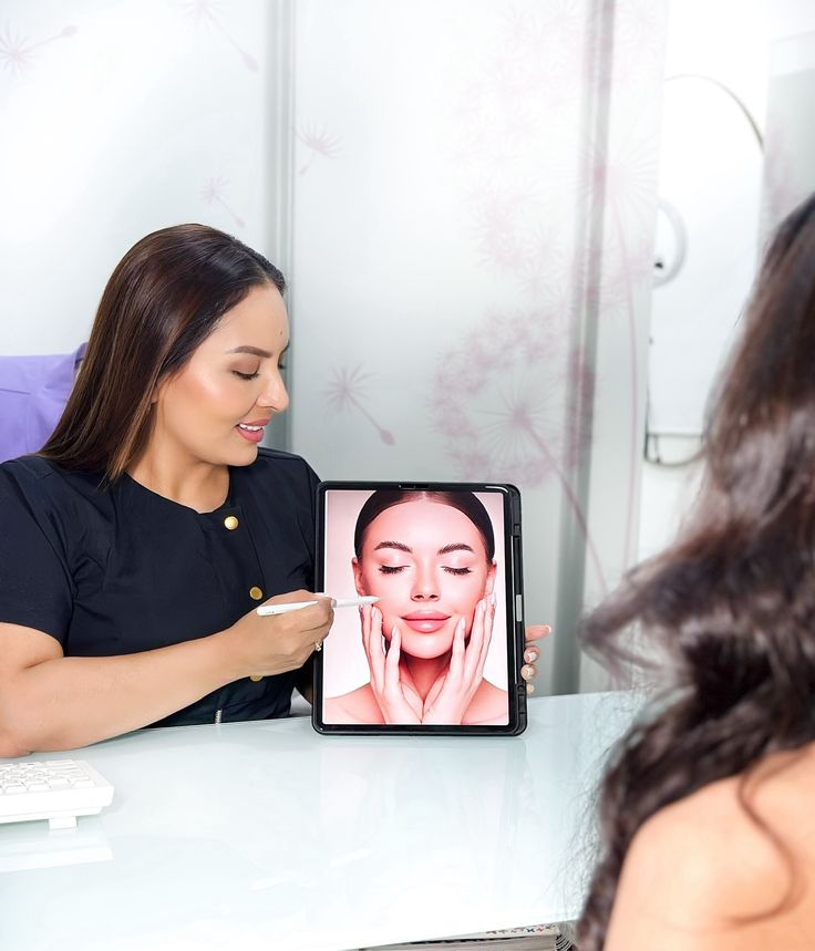 Beauty consultant discussing skincare with client, showcasing facial treatment on tablet in modern clinic.