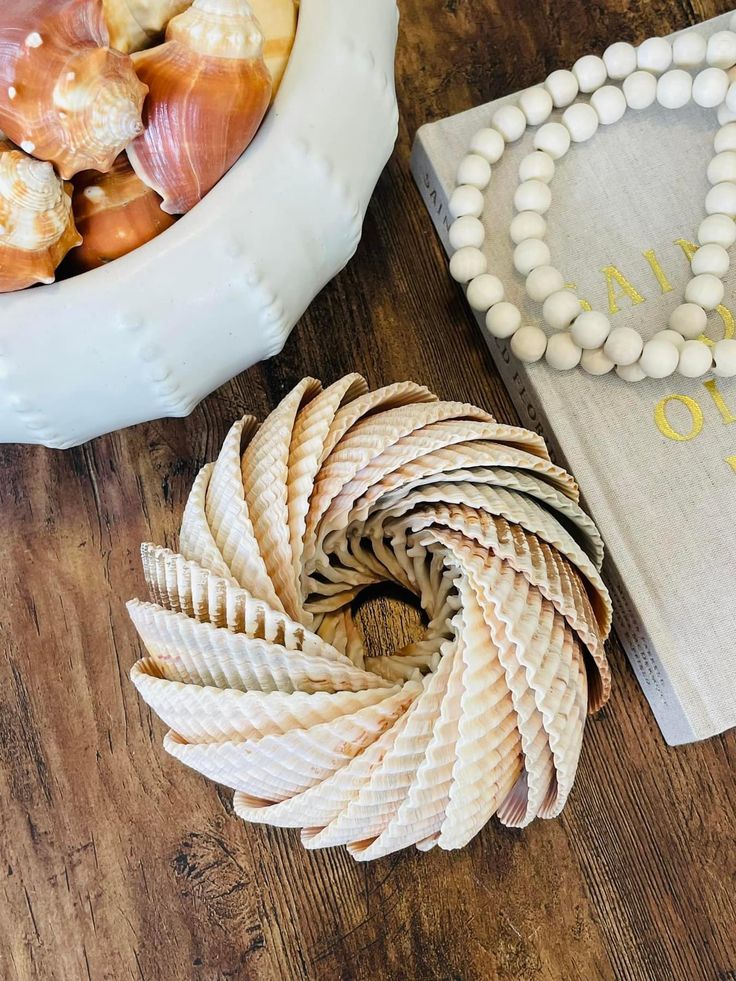 Shell arrangement on table with decorative beads and book, featuring unique spiral design and rustic coastal decor elements.