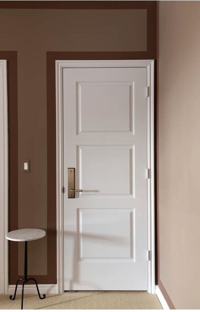 White paneled door in a brown room with a marble-top side table, beige carpet.