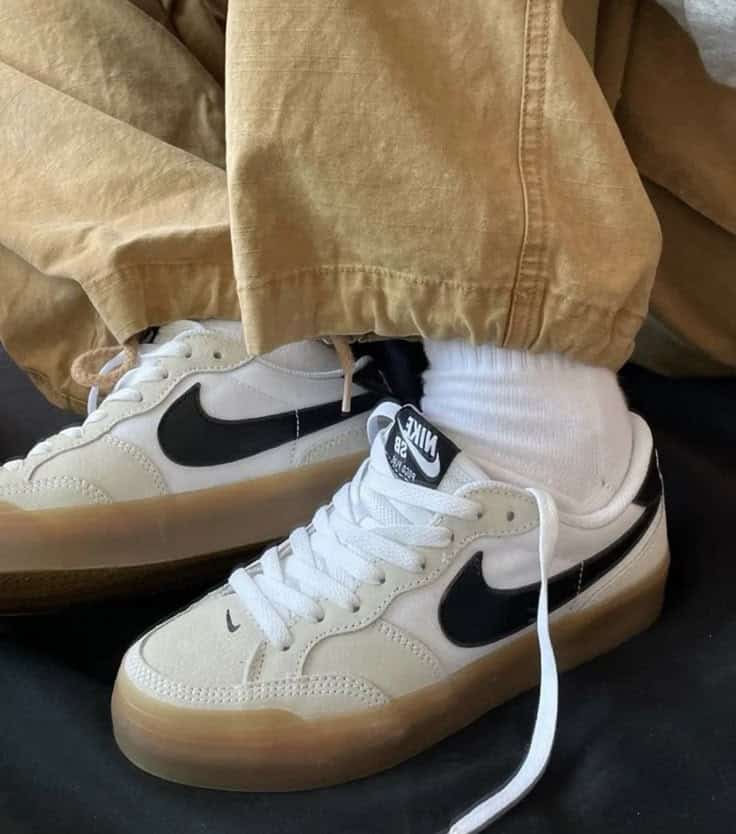 White Nike sneakers with black swoosh, brown pants, and white socks for a casual style.