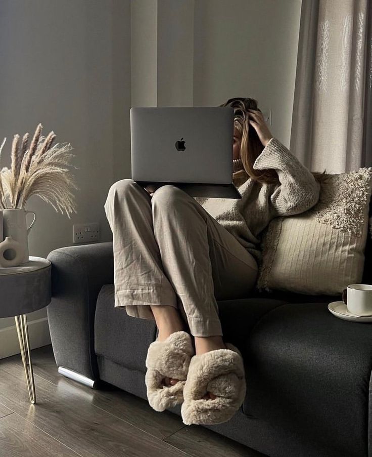 8552c576-20d4-4c90-bb4d-70df77e5931f Cozy home office setting with person in fluffy slippers using a laptop on a couch, next to coffee and pampas grass. | Sky Rye Design Cozy home office setting with person in fluffy slippers using a laptop on a couch, next to coffee and pampas grass.