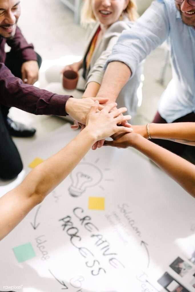 Team collaborating on creative process, hands joined over a plan chart with lightbulb sketch, signifying teamwork.