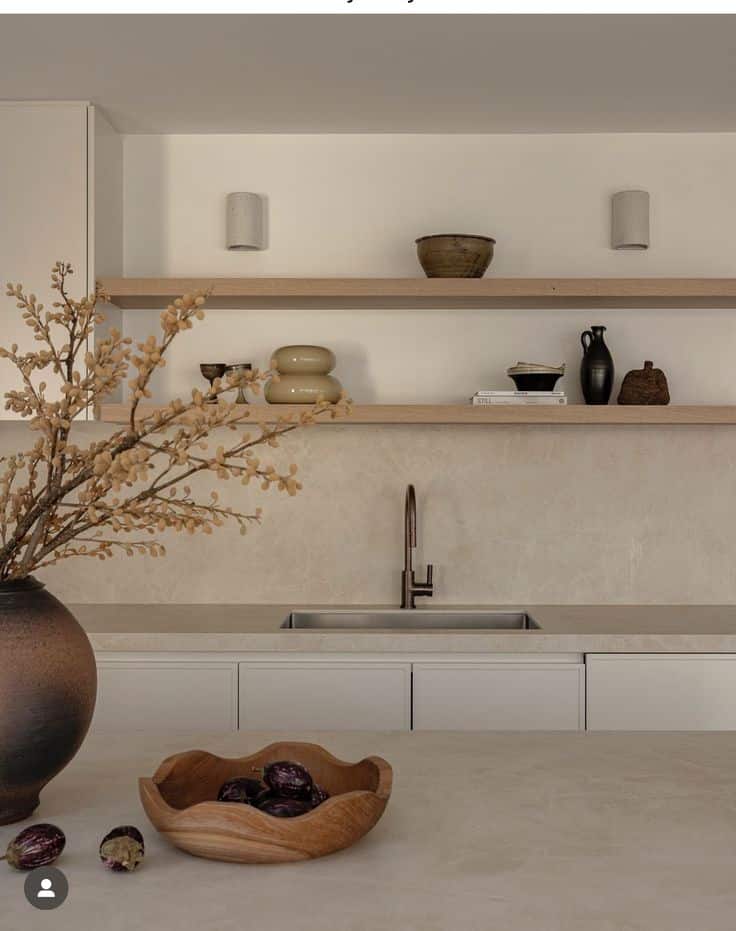 Minimalist kitchen with open shelves, earthy decor, and a sleek countertop featuring a wooden bowl with fresh produce.
