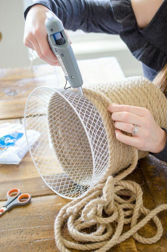 Person crafting rope basket with glue gun on wooden table.
