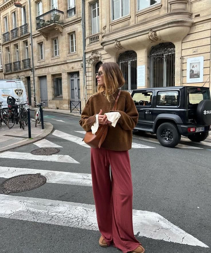 Fashionable woman wearing wide-leg pants and oversized sweater on a city street. Urban style streetwear.