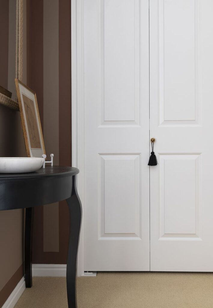 Elegant hallway with a white double door and a black table featuring a framed artwork and decorative bowl.